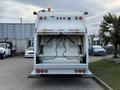 A 2010 Autocar Xpeditor waste collection truck viewed from the rear with its lifting mechanism exposed and equipped with red and amber lights