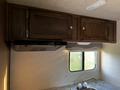 A wooden cabinet with two doors mounted above a kitchen area featuring a small sink and a countertop