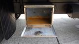 An open storage compartment mounted on the side of a truck revealing a rusty interior and a metal base where equipment may be secured