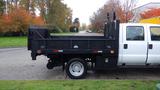 A 2011 Ford F-550 truck with a flatbed and black tool boxes on the side is parked on the street