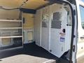 Interior of a 2016 Ford Transit showing shelving on one side and a white partition with a mesh window attached to the opposite wall