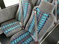 Two rows of gray bus seats with blue patterned fabric and seatbelts designed for safety