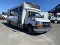 A 2020 Chevrolet Express bus with a white exterior and large windows parked at an angle showcasing its front and side profile