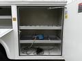 A 2001 Ford F-350 with an open compartment featuring metal shelves and various tools including a blue hose and black cords on the bottom shelf