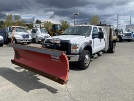 A 2010 Ford F-550 truck equipped with a large red snow plow mounted on the front