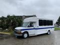 A 2015 Chevrolet Express van in white with a blue stripe on the side parked on a wet surface with visible wheels and windows