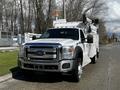 A 2016 Ford F-550 utility truck with a ladder, white body, and orange safety light on top parked on a street