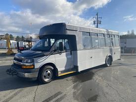 A 2018 Chevrolet Express van with a gray front and white body featuring large windows and a flat roof designed for passenger transport