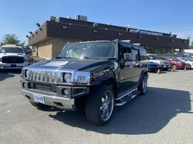 A black 2003 Hummer H2 with chrome accents parked on a lot featuring a distinctive boxy shape and oversized wheels