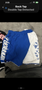 Blue and white MMA shorts with "WARRIOR" printed on one side and a design featuring multiple logos or patterns on the other side
