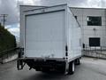 A white 2018 Isuzu NPR box truck with a plain rear and no visible markings positioned in the foreground