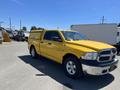 A yellow 2015 RAM 1500 pickup truck with a matching camper shell in the bed is parked on a lot