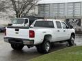 A white 2013 Chevrolet Silverado 3500HD pickup truck with four doors and a black truck bed is parked, showcasing its chrome wheels and rear view