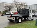 A 2019 Freightliner M2 flatbed truck with a black flatbed and metal railing on the back is parked on a wet surface
