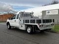 A 2014 Ford F-250 SD truck with a flatbed and metal storage compartments on the back parked on a street