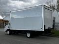 A white 2022 Isuzu NPR box truck with a large cargo area and a flatbed rear, parked on a pavement surface