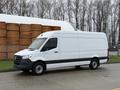 A 2019 Mercedes-Benz Sprinter van in white with a black lower section parked on a road with a storage area in the background