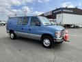 A blue 2009 Ford Econoline van is parked with a traffic cone in front of it and a roof rack on top
