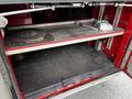 A 1991 Sutphen Deluge fire truck storage compartment with metal shelves displaying a circular saw blade a metal wrench and a rolled canvas tool bag