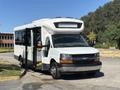 A 2017 Chevrolet Express bus with a white exterior and open side doors parked on a roadway