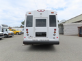 A 2020 Chevrolet Express bus with a white body and rear door displaying warning lights and a message that reads PLEASE YIELD THANKS FOR THE BRAKE