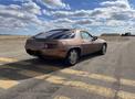 A metallic brown 1983 Porsche 928 is parked on a road with a distinct shape and features a sleek design and distinctive rear lights