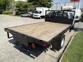 A 2018 Ford F-550 featuring a flatbed with a wooden surface and a black frame visible from the rear angle