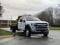 A 2022 Ford F-550 truck with a flatbed body parked on a wet surface, showcasing its front profile and dual rear wheels