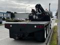 A black 2006 Freightliner M2 112 flatbed truck with a metal mesh back and hydraulic equipment mounted on top