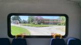 The image shows a 2011 Chevrolet Express viewed through a window with seats in the foreground and a school building visible outside