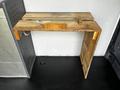 A wooden table made from reclaimed materials positioned against a wall inside a vehicle with a metal surface nearby
