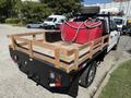 A 2019 Ford F-350 SD with a flatbed featuring wooden railings and a red fuel tank attached to the side along with a hose and spare tire on the bed
