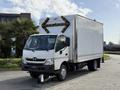 A 2014 Hino 195 delivery truck with a white body and black accents featuring a large cargo box with a triangular warning light on the rear