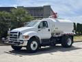 A white 2015 Ford F-750 water truck features a cylindrical tank mounted on the chassis with a hose attachment and visible water signage on the side