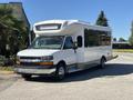 A 2017 Chevrolet Express bus with a white exterior and large side windows parked on a pathway