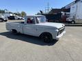 A 1962 Ford F-100 with a grey body, black wheels, and red interior accents parked in a lot