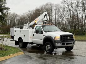 A white 2006 Ford F-450 truck with an elevated work platform and a toolbox mounted in the bed