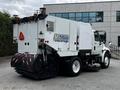 A white 2012 International DuraStar 4300 street sweeper with a large rear broom and various warning lights mounted on top