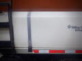 A white tank secured with a gray strap on a truck with visible branding and red reflective strips on the side