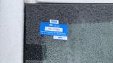 A blue vehicle registration sticker with the text "2025" and "CERTIFICATE OF APPROVAL" on a wet surface with droplets of water