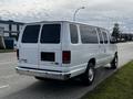 A white 2014 Ford Econoline van parked on the roadside showing its rear view with large windows and a chrome bumper