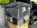 A portable cooler with a gray exterior and adjustable handles is positioned on a wooden base inside a vehicle