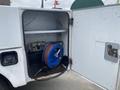 An open compartment of a 2003 Ford F-450 SD showing a large blue reel with hoses and a pump system inside