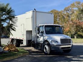 A white 2011 Freightliner M2 106 box truck with a large cargo area and a tall exhaust pipe parked on a street
