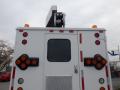 A white 2002 International 4700 truck with an elevated platform and various lights and directional signals on its rear