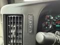 Close-up of the dashboard controls of a 2014 GMC Savana featuring buttons for lighting and ventilation with a speedometer and other gauges in the background