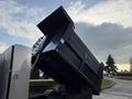 A 2015 Isuzu NPR HD with a dump trailer raised at an angle showcasing the open bed and black exterior