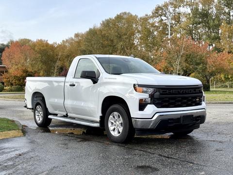 A 2024 Chevrolet Silverado 1500 pickup truck in white with a black grille and chrome accents parked on a wet surface