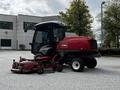 A 2012 Toro Groundsmaster is parked with a red exterior and enclosed cab featuring a large front glass windshield and a mowing deck attached at the front