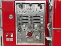 A silver control panel with various gauges levers and knobs used for operating a fire truck system